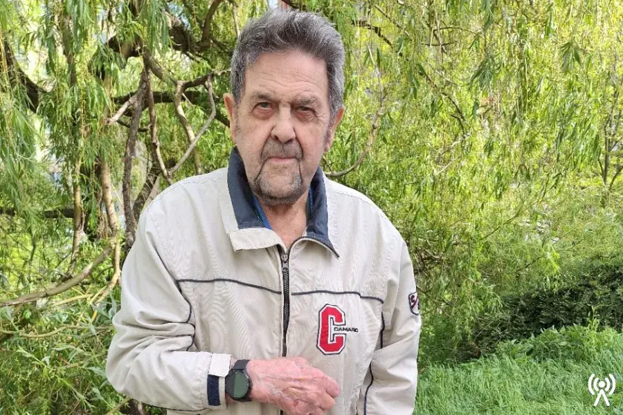 JAK TÍSŇOVÁ PÉČE ANDĚL STRÁŽNÝ POMÁHÁ SENIORŮM: PŘÍBĚH PANA VÁCLAVA Z ŽELEZNICE 1 Pan Václav, senior a klient tísňové péče Anděl Strážný, s monitorovacími hodinkami na ruce, stojí venku před zeleným keřem.